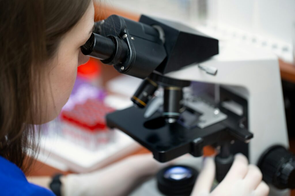 Young attractive veterinary worker in gloves using microscope for testing blood samples of animals.