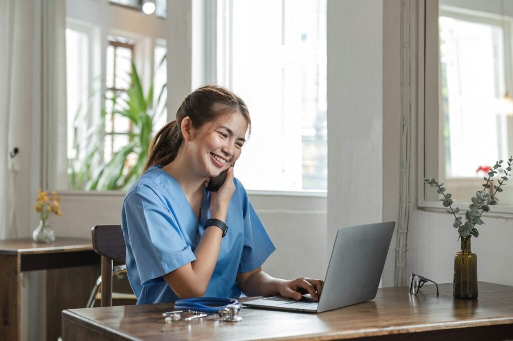 Happy female doctor using laptop to do data work and chat with patients on the phone in office in